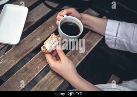 Cup of coffee and eclair on a wooden table close-up. Stock Photo