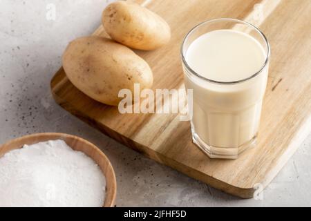 Powdered vegan potato milk glass close up, potato powder and tubers on concrete backdrop. Non dairy alternative milk. Vegetable milk replacer. Selecti Stock Photo