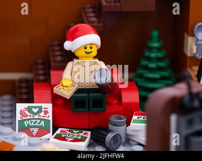 Tambov, Russian Federation - January 03, 2022 A Lego man wearing a christmas hat sitting on a red couch eating a pizza and watching television with pi Stock Photo
