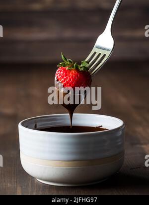 Close up of a strawberry dipped in melted chocolate, against a dark background. Stock Photo