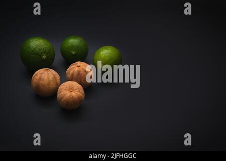 Fresh dark green and sun dried organic fruits of Loomi or Black Lime, Black Lemon, Omani Lemon on black background. Stock Photo