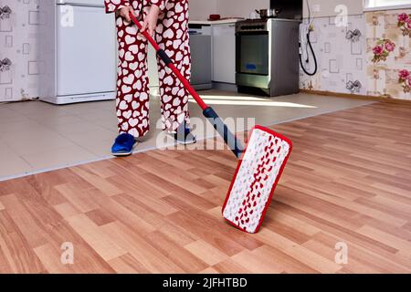 Using flat mop with microfiber pad to mopping floor in kitchen during housework. Stock Photo