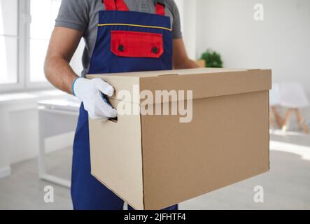 Large cardboard box with things in hands of male employee of moving and delivery company. Stock Photo