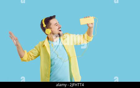 Cheerful carefree man in headphones sings favorite song and uses mobile phone as microphone. Stock Photo