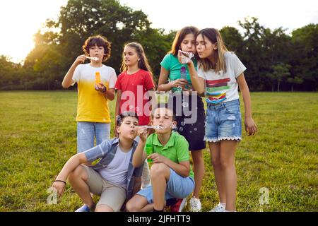 Children teens boys and girls posing in summer park and blowing bubbles having fun with friends Stock Photo