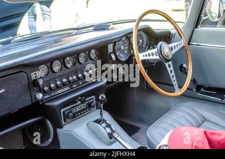 View of the interior dashboard of a classic E-Type jaguar car with a wooden steering wheel and lines of switches and gauges. Stock Photo