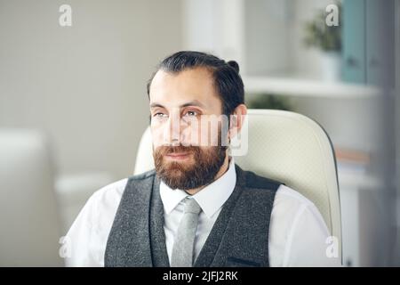 Content busy handsome young business manager with beard sitting in office and looking at computer monitor Stock Photo