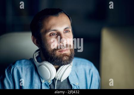 Close-up of thoughtful bearded computer programmer with headphones on neck looking at computer monitor while examining code Stock Photo