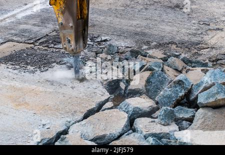 Close-up of demolition hammer with dust and sparks and broken concrete pieces. Detail of hydraulic jackhammer mounted on excavator arm. Repair working. Stock Photo