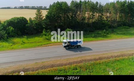 Flight over the straight road with driving truck on a sunny summer day. Scene. Aerial view of amazing natural landscape with farm fields. Stock Photo