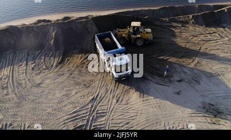 USA, California - May 20, 2022: excavator digging and loading sand into dump truck at river bank. Scene. Heavy machinery working at sand quarry. Stock Photo