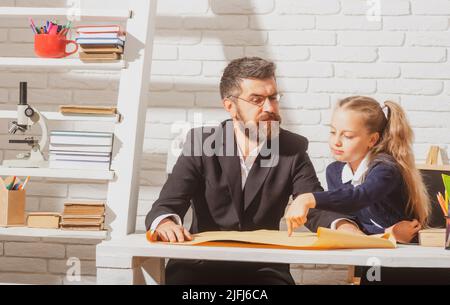 Elementary funny pupil girl with serious teacher in classroom. Fathers and daughters learning. Doing homework with dad Stock Photo