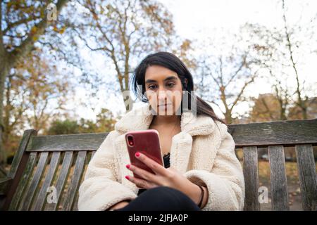 Girl wears earphones and listens to a podcast while using her smartphone Stock Photo