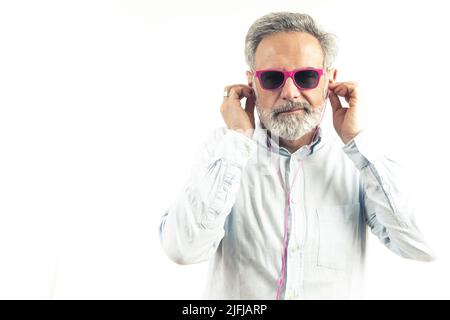 grey-haired Caucasian man in pink sunglasses listens to music in pink earphones white background studio shot copy space indoors . High quality photo Stock Photo