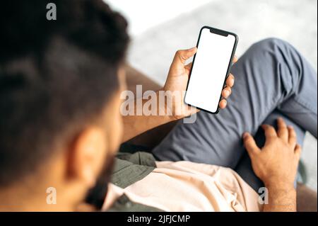 Gadgets and technologies concept. Modern smartphone with a blank white mockup screen for presentations, advertising, your text, in male hands. Top view Stock Photo