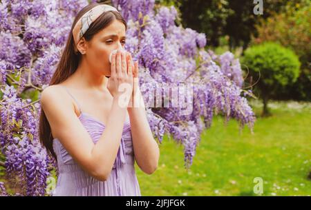 Girl with nose allergy sneezing. Polen illnes symptom concept. Woman allergic to blossom during spring blooming tree outdoor Stock Photo