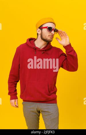 Young pensive handsome caucasian man in Great Britain flag sunglasses and casual wear, looking away isolated on yellow background. Stylish bearded smart hipster man casual look. Stock Photo