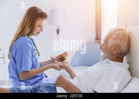 elderly man senior people lay on bed health care giving medicine pills from nurse at homecare Stock Photo