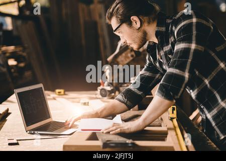 builder wood worker wooden furniture maker using laptop computer to design project Stock Photo