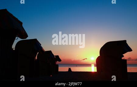 Timmendorfer Strand, Germany. 04th July, 2022. A young couple sits on the beach between beach chairs and enjoys the sunrise. Credit: Christian Charisius/dpa/Alamy Live News Stock Photo