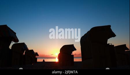 Timmendorfer Strand, Germany. 04th July, 2022. A young couple sits on the beach between beach chairs and enjoys the sunrise. Credit: Christian Charisius/dpa/Alamy Live News Stock Photo