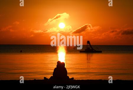 Timmendorfer Strand, Germany. 04th July, 2022. A young couple sits on the beach between beach chairs and enjoys the sunrise. Summer vacation has begun in Schleswig-Holstein and Mecklenburg-Western Pomerania. Credit: Christian Charisius/dpa/Alamy Live News Stock Photo