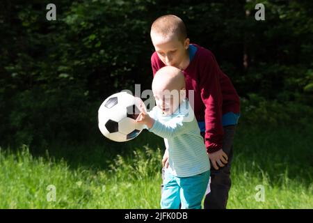 Two boys in blue and magenta shirt playing in forest glade with soccer ball. Childhood concept Stock Photo