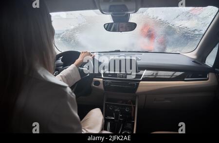 Back view of young woman client sitting in the car on carwash station. Worker cleaning automobile, using high pressure water. Stock Photo