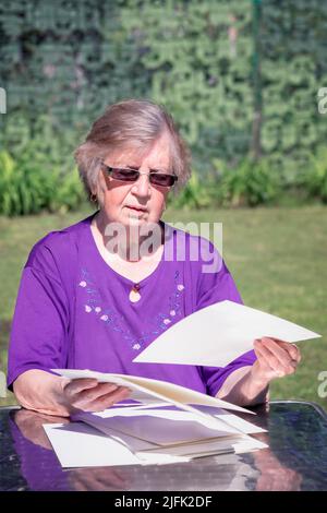 Elderly woman sorting through papers while sitting outdoor. Stock Photo