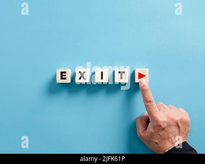 Male hand presses the play button with the word exit on wooden cubes. Starting exit strategy in business concept. Stock Photo