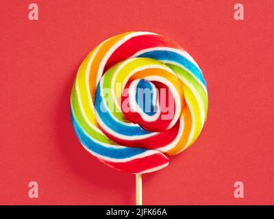 Rainbow colored swirl round candy lollipop on red background. Close up macro. Stock Photo