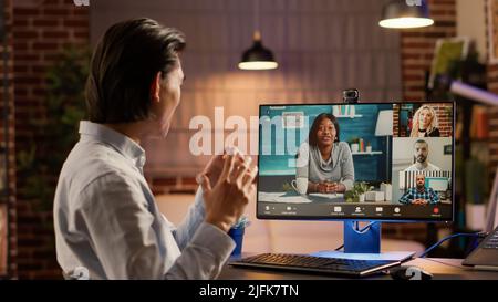 Asian man attending videocall meeting with group of people on computer webcam, having remote conversation online. Videoconference call for telecommunications and telework, teleconference. Stock Photo