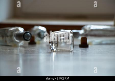 A glass and empty alcohol bottles lie on the floor in an apartment in the dark, alcoholism and bad habits, glass bottles and a glass of vodka Stock Photo