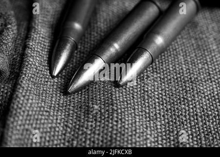 Three Ak-47 cartridges lying on a piece of military canvas, monochrome photo Stock Photo