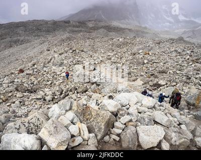 Trekkers and porters traversing  the moraine near Gorak Shep on the  Everest Base Camp trek from Lobuche, Khumbu Stock Photo