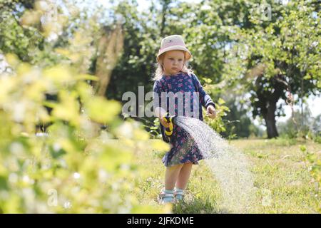 Adorable little girl playing with a garden hose on hot and sunny summer day Stock Photo