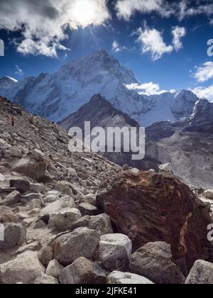 Trekkers follow the rocky path along the Khumbu Glacier's moraine below Nuptse Nup II (7732m) on the Everest Base Camp route near Gorak Shep. Stock Photo