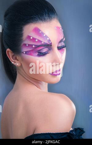 Beautiful Caucasian woman with purple face painting and crystals on her face looking over the shoulder on a blue background Stock Photo