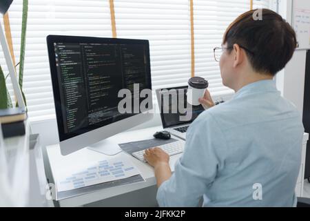 Software development concept, Male programmer checking website programming and drinking coffee. Stock Photo