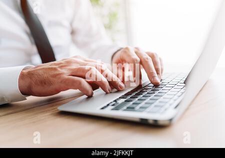 Businessman using laptop computer, hands typing keyboard at office desk, closeup with selective focus Stock Photo