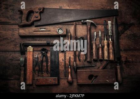 craftsmanship concept illustrated by collection of old carpentry tools on wooden workbench with chisel, spirit level, pincers, handsaw, screwdriver Stock Photo