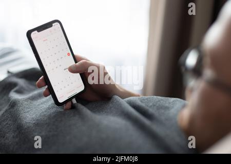 Man laying on a couch and looking calendar on his mobile phone. Stock Photo