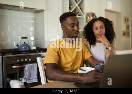 Young multiethnic couple using a laptop during breakfast at a kitchen table Stock Photo