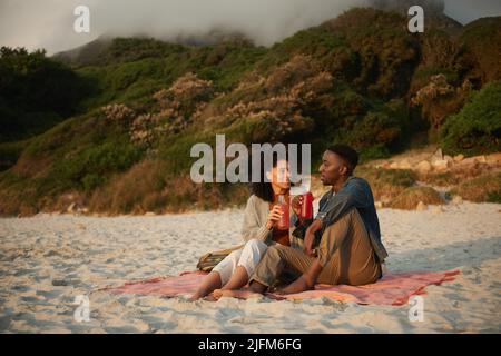 Smiling young multiethnic couple talking on a sandy beach at sunset Stock Photo