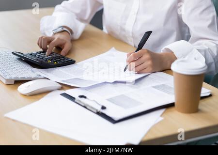 Close-up photo of a business woman's hand on paper work, an accountant calculates and summarizes the results of the financial year with a calculator, an Asian woman works in the office. Stock Photo