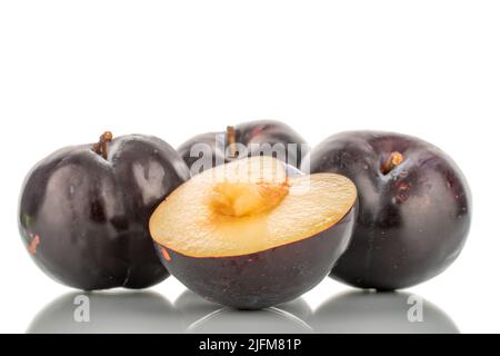 Three whole and one half sweet tasty dark purple plums, close-up, isolated on white. Stock Photo