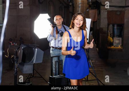 Young attractive woman delighted with professional photo shooting on town street with male photographer Stock Photo