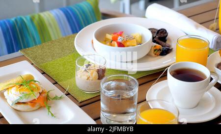 Hotel table with breakfast food. Served meal in modern tropical resort. Dinner for two in restaurant with fresh fruits, juices, eggs and cereals Stock Photo