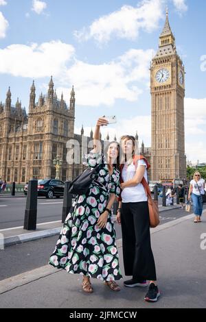 Tourists pose for a selfie with Elizabeth Tower and the Houses of Parliament, in Westminster, London, as people enjoy the warm weather. Picture date: Monday July 4, 2022. Stock Photo