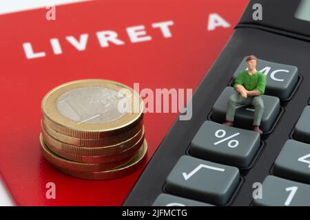 Figurine sitting on a calculator near a stack of euro coins and a French livret A. Concepts of inflation, savings and livret A interest rates Stock Photo